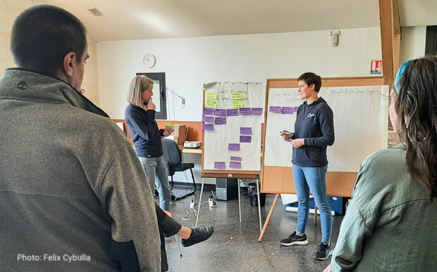 Four people discussing in front of a flipchart with post-it notes at the CCNet Europe pause-and-reflect